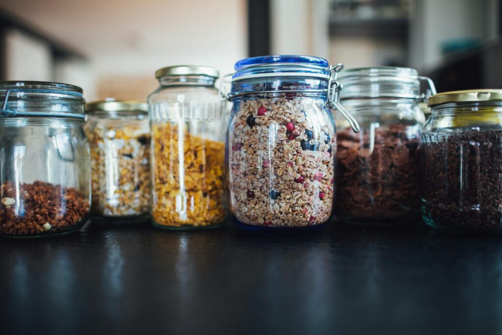 Close-up of various cereals in glass jars on a kitchen counter, showcasing diverse breakfast options.