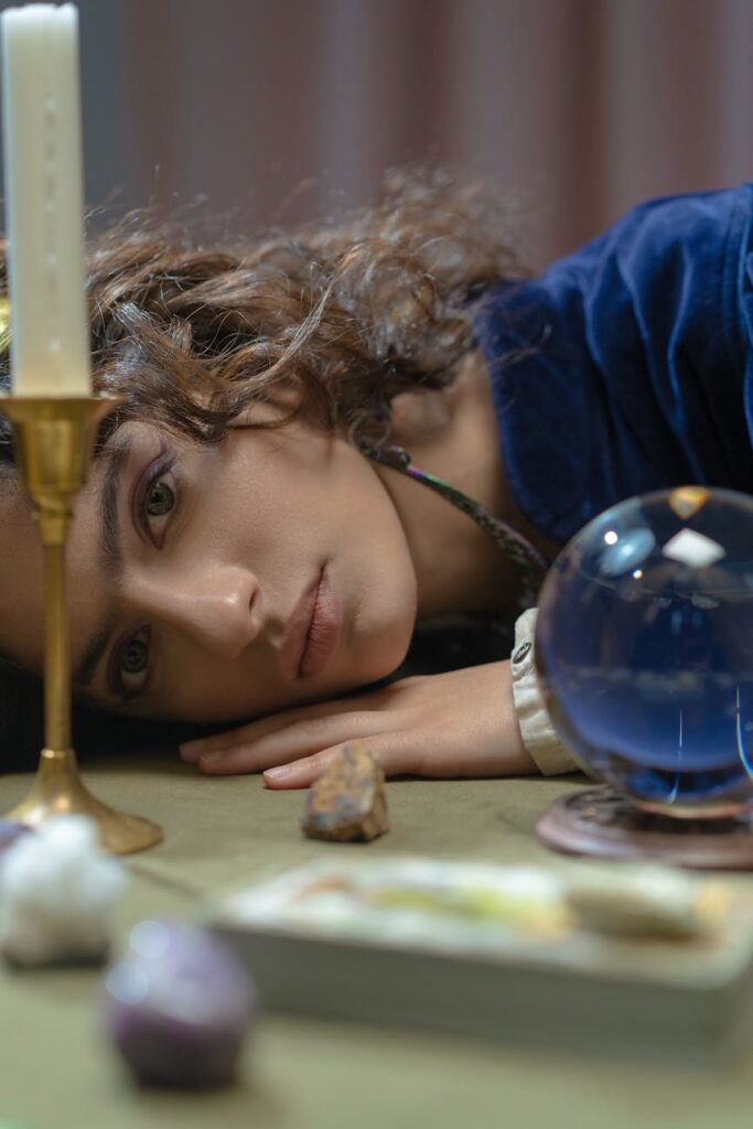 a woman resting her head on a table with a candle and glass ball